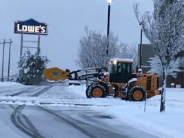 Commercial snow removal in progress at a Lowe's store, featuring a snowplow clearing a snowy parking lot.