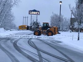 Commercial snow removal equipment clearing a snowy parking lot near a Lowe's store, showcasing McLeod Landscaping's snow management services.