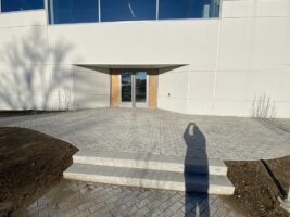 Commercial landscaping installation featuring a stone walkway and steps leading to a modern building entrance, showcasing McLeod Landscaping's hardscaping services.