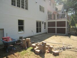 Residential landscaping project with a newly constructed patio area, featuring stacked bricks, a wheelbarrow, and tools, showcasing McLeod Landscaping's hardscape services.