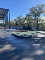 Commercial landscaping installation featuring a circular garden bed with greenery, surrounded by a paved area and trees, showcasing McLeod Landscaping's design services.
