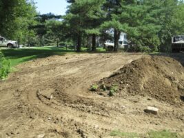Residential landscaping project site showing freshly graded earth, mounds of soil, and surrounding greenery, highlighting McLeod Landscaping's preparation for design and construction.