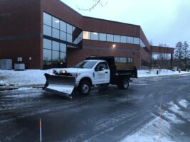 Commercial snow removal truck clearing snow outside a commercial building, showcasing McLeod Landscaping's snow management services.