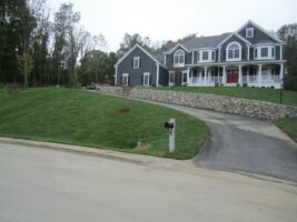 Residential landscaping project by McLeod Landscaping featuring a well-manicured lawn, stone wall, and a modern home exterior.