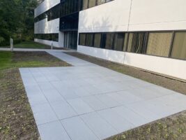 Commercial landscaping project featuring a newly installed gray paver walkway adjacent to a modern building, showcasing McLeod Landscaping's hardscaping services.