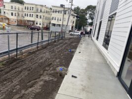Commercial landscaping project showcasing freshly prepared soil along a sidewalk, with construction materials and equipment visible, illustrating McLeod Landscaping's services.