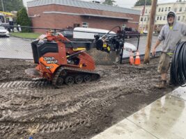 Excavator on muddy terrain with worker, illustrating commercial landscaping project by McLeod Landscaping.