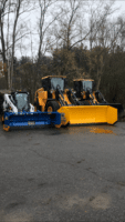 Commercial snow removal equipment, including yellow and blue snow plows, parked in an outdoor setting, showcasing McLeod Landscaping's snow management services.