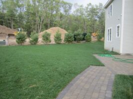 Residential landscaping project featuring a well-maintained green lawn, bordered by a stone pathway and shrubs, with construction materials visible in the background, showcasing McLeod Landscaping's design and construction services.