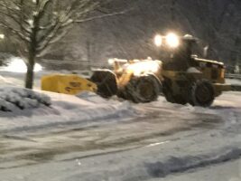 Commercial snow removal equipment clearing snow from a parking lot at night, showcasing McLeod Landscaping's snow management services.