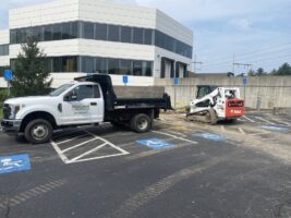 Commercial landscaping work in progress, featuring McLeod Landscaping truck and equipment in a parking lot near a modern office building.
