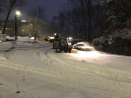 Commercial snow removal service by McLeod Landscaping, snow-covered parking lot with snowplow clearing snow at night.