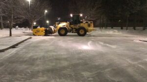 Commercial snow removal equipment clearing a snow-covered parking lot at night, showcasing McLeod Landscaping's snow management services.