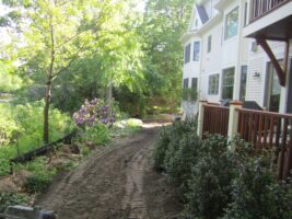 Residential landscaping project featuring a well-defined pathway alongside a house, bordered by lush greenery and flowering plants, highlighting McLeod Landscaping's design and construction expertise.