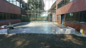 Commercial landscaping project featuring a newly installed paver patio and retaining walls outside a modern building, showcasing McLeod Landscaping's hardscaping services.