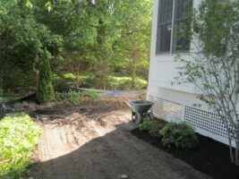 Residential landscaping project featuring freshly prepared soil, wheelbarrow, and surrounding greenery, showcasing McLeod Landscaping's design and construction services.