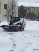 Commercial snow removal equipment clearing a snowy residential driveway, showcasing McLeod Landscaping's snow management services.
