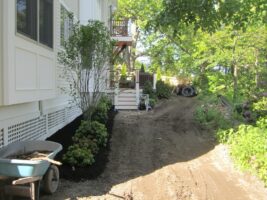 Residential landscaping project featuring freshly mulched flower beds, a wheelbarrow, and a dirt pathway next to a home, showcasing McLeod Landscaping's design and construction services.
