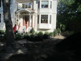 Residential landscaping project by McLeod Landscaping featuring a newly designed garden area with shrubs and mulch near a two-story house.