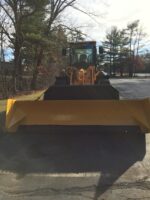 Commercial snow removal equipment, featuring a front-end loader with a large yellow snow plow, positioned on a paved surface surrounded by trees, highlighting McLeod Landscaping's snow management services.