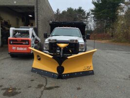 Commercial snow removal truck with a yellow snow plow, parked in front of a building, showcasing McLeod Landscaping's snow management services.