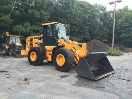 Commercial snow removal equipment, including a yellow loader with a large front bucket, parked in a landscaping yard, showcasing McLeod Landscaping's snow management capabilities.
