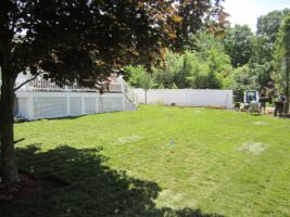 Residential landscaping project showcasing a well-maintained green lawn, shaded by a tree, with a white fence and patio area in the background, highlighting McLeod Landscaping's expertise in outdoor design.