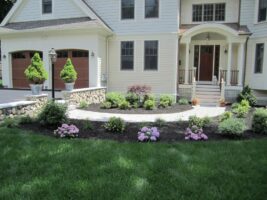 Residential landscaping featuring a well-maintained front yard with flower beds, decorative shrubs, and a stone pathway leading to a home entrance, showcasing McLeod Landscaping's design expertise.
