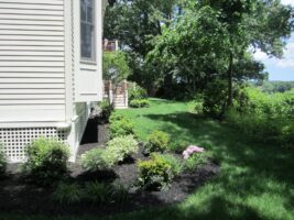 Residential landscaping project by McLeod Landscaping featuring well-maintained flower beds, lush green lawn, and a tree-lined background.