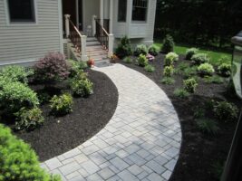 Residential landscaping with a curved stone pathway leading to a home entrance, surrounded by well-maintained flower beds and shrubs, showcasing McLeod Landscaping's design expertise.