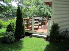 Residential landscaping featuring a wooden deck with outdoor furniture, surrounded by manicured shrubs and trees, showcasing McLeod Landscaping's design and construction expertise.