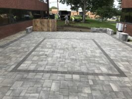 Commercial hardscaping installation featuring a newly paved patio area with a border design, surrounded by landscaping work in progress.