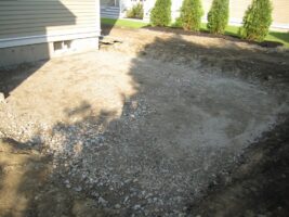 Residential landscaping project site with gravel base, surrounded by greenery and a house foundation, showcasing preparation for landscaping by McLeod Landscaping.