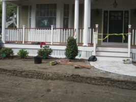 Residential landscaping project featuring newly planted shrubs, tools, and preparation for hardscaping in front of a house with a porch.