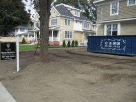 Residential landscaping project featuring a cleared yard with a construction dumpster, adjacent to two newly built houses, showcasing McLeod Landscaping's work in outdoor design and construction.