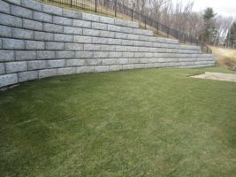 Residential landscaping project featuring a curved stone retaining wall and well-maintained green lawn, showcasing McLeod Landscaping's hardscape design expertise.