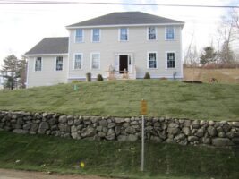 Residential landscaping project by McLeod Landscaping featuring a two-story home with freshly laid sod and a stone wall, highlighting quality landscaping design and construction services.