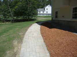 Curved stone walkway leading to a landscaped area with mulch, adjacent to a residential home, showcasing McLeod Landscaping's design and hardscape work.