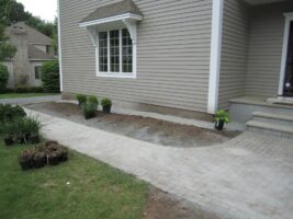 Residential landscaping project featuring a paved walkway leading to a home, with freshly planted shrubs and plants arranged along the path, showcasing McLeod Landscaping's design and construction services.