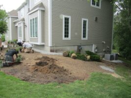 Residential landscaping project in progress, featuring workers installing plants and preparing soil near a home, showcasing McLeod Landscaping's design and construction services.