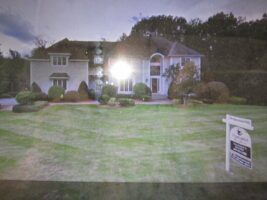 Residential landscaping project showcasing a well-maintained lawn and ornamental shrubs around a two-story house, with a for-sale sign prominently displayed.