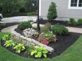 Residential landscaping featuring a stone border garden with colorful flowers, shrubs, and ornamental plants, complemented by a lamp post and well-maintained lawn, showcasing McLeod Landscaping's design expertise.