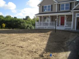 Residential landscaping project by McLeod Landscaping featuring a newly prepared yard with sandy soil in front of a two-story house, showcasing the potential for future landscaping design and construction.