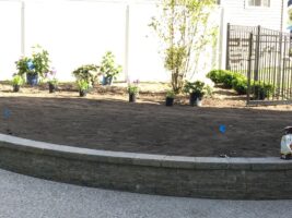 Residential landscaping project by McLeod Landscaping featuring newly prepared planting area with flower pots and surrounding greenery.