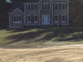 Residential landscaping project featuring a two-story house with a well-maintained lawn and a dirt driveway, showcasing McLeod Landscaping's design and construction capabilities.