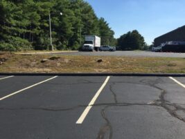 Parking lot with marked spaces and commercial vehicles in the background, showcasing a professional landscaping project area by McLeod Landscaping.