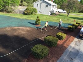 Two workers watering freshly landscaped area with shrubs and mulch, showcasing McLeod Landscaping's residential project.