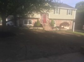 Residential landscaping project by McLeod Landscaping featuring a two-story home with a red front door, stone steps, and well-maintained greenery in the yard.