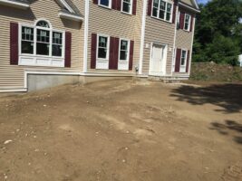 Residential landscaping project featuring a newly prepared yard area in front of a house with beige siding and maroon shutters, showcasing the groundwork for future landscaping by McLeod Landscaping.
