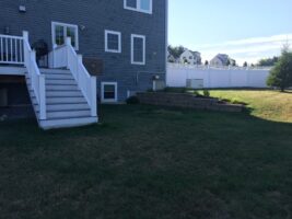 Residential backyard featuring a well-maintained lawn, stone retaining wall, and white wooden stairs leading to a house, illustrating landscaping project by McLeod Landscaping.